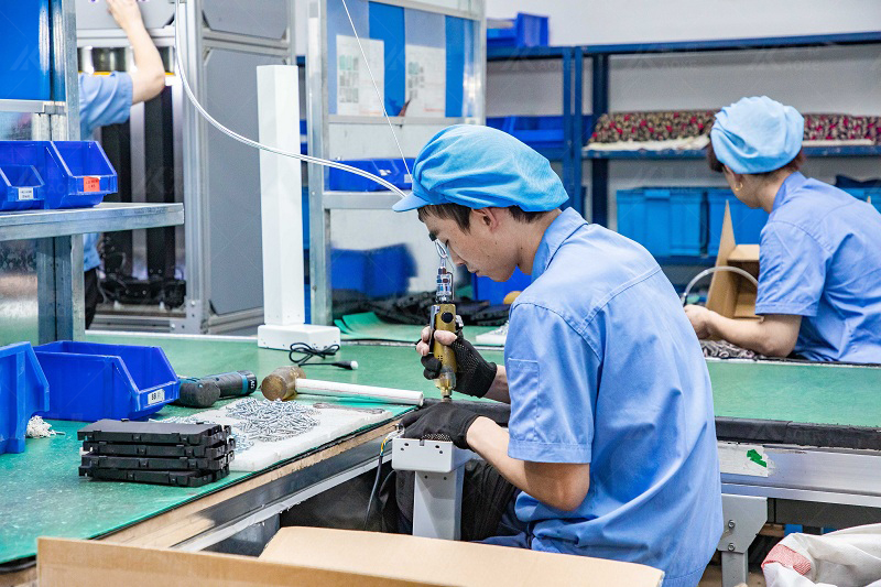 The workers are tightening the screws on the table frames on the assembly line